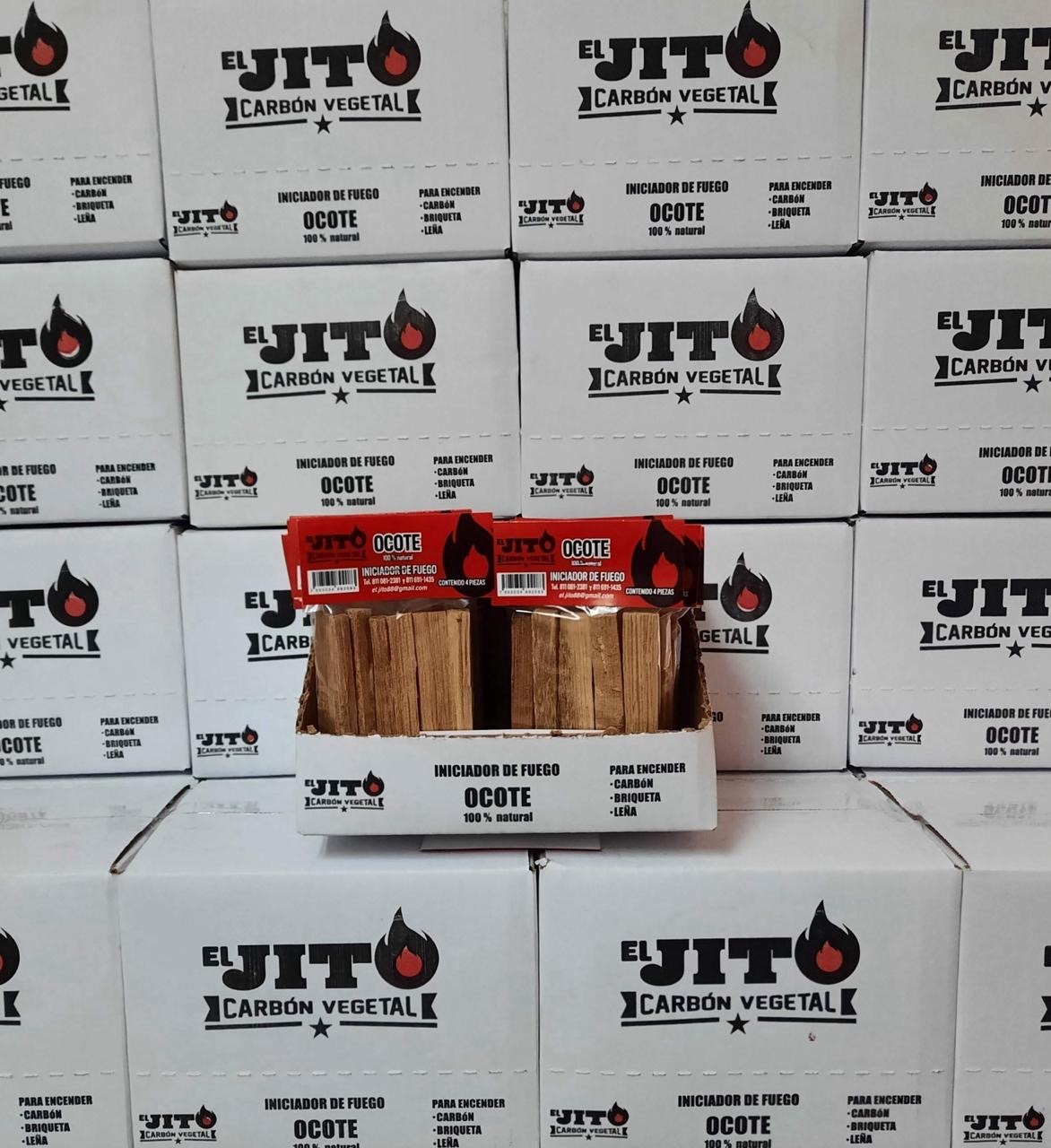 Pilas de cajas blancas con logotipos negros y rojos de "El Jito Carbón Vegetal" rodean una exhibición de encendedores de madera con la etiqueta "Ocote" en el centro. Los paquetes de iniciadores de fuego se destacan y muestran piezas de madera cuidadosamente dispuestas.